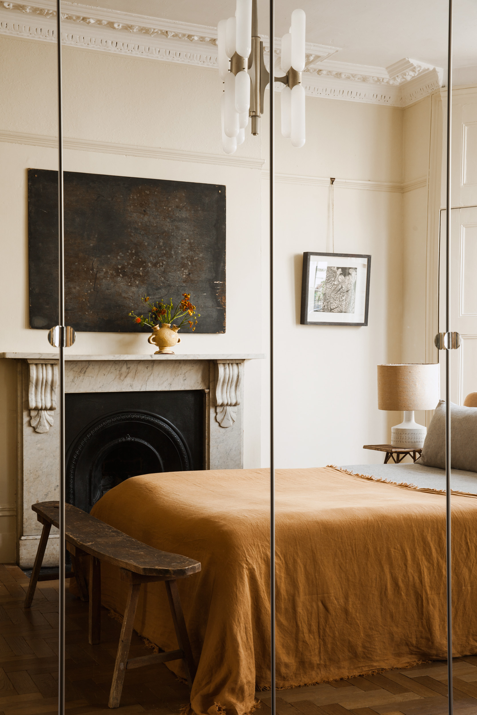 Bedroom fireplace reflected beside the plain ochre bedspread