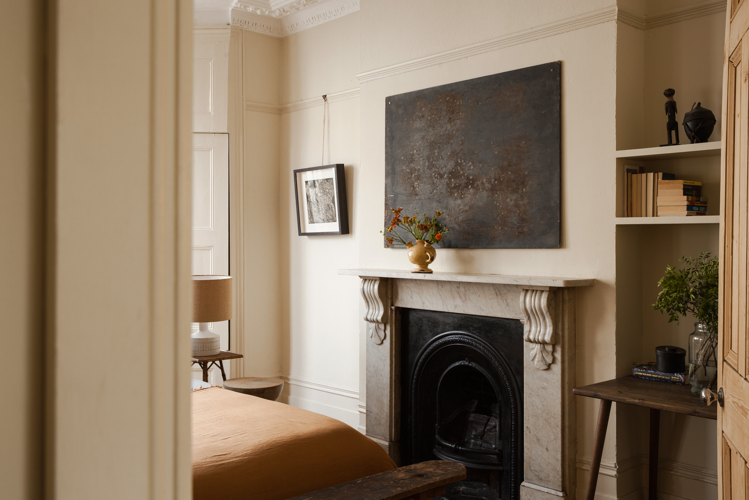 View into the bedroom with a plain ochre bedspread and marble fireplace