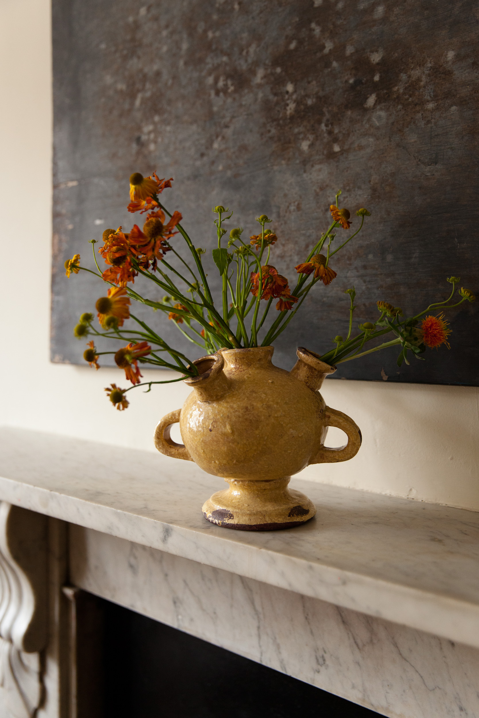Ochre ceramic vase with orange flowers on the bedroom marble mantelpiece