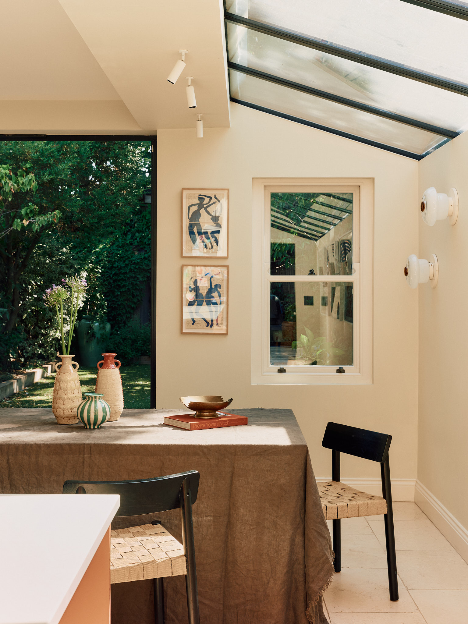 Sunlit dining room with a glazed roof, timber table and framed art at School House