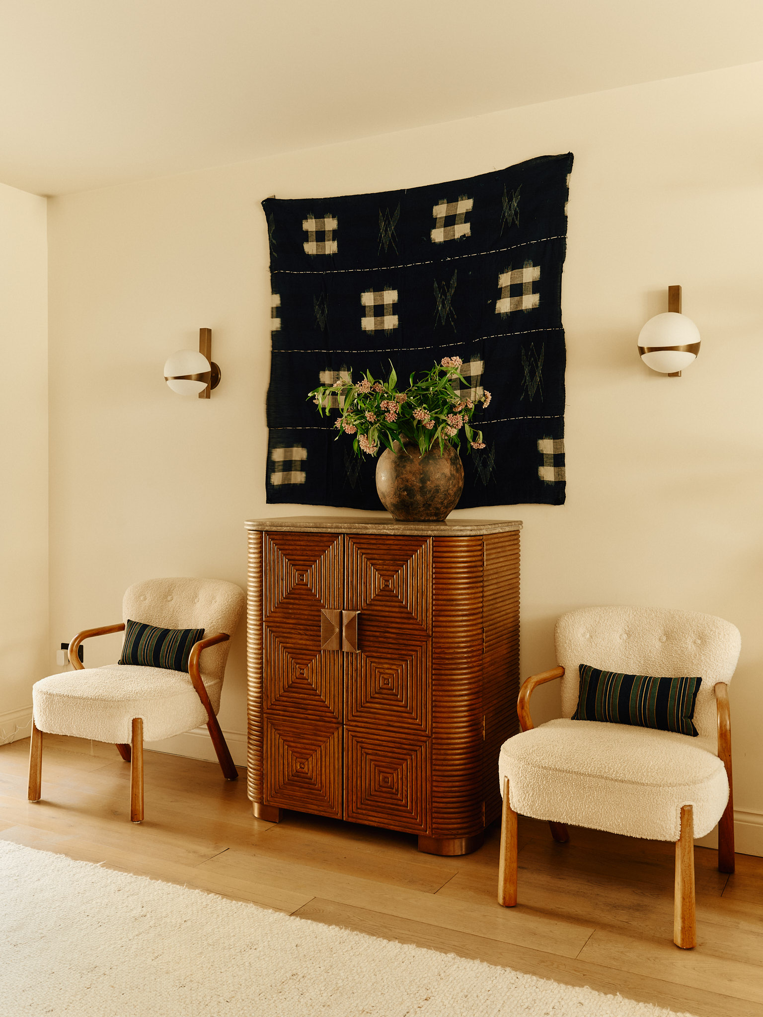 Timber cabinet and paired chairs beneath a dark textile artwork at School House
