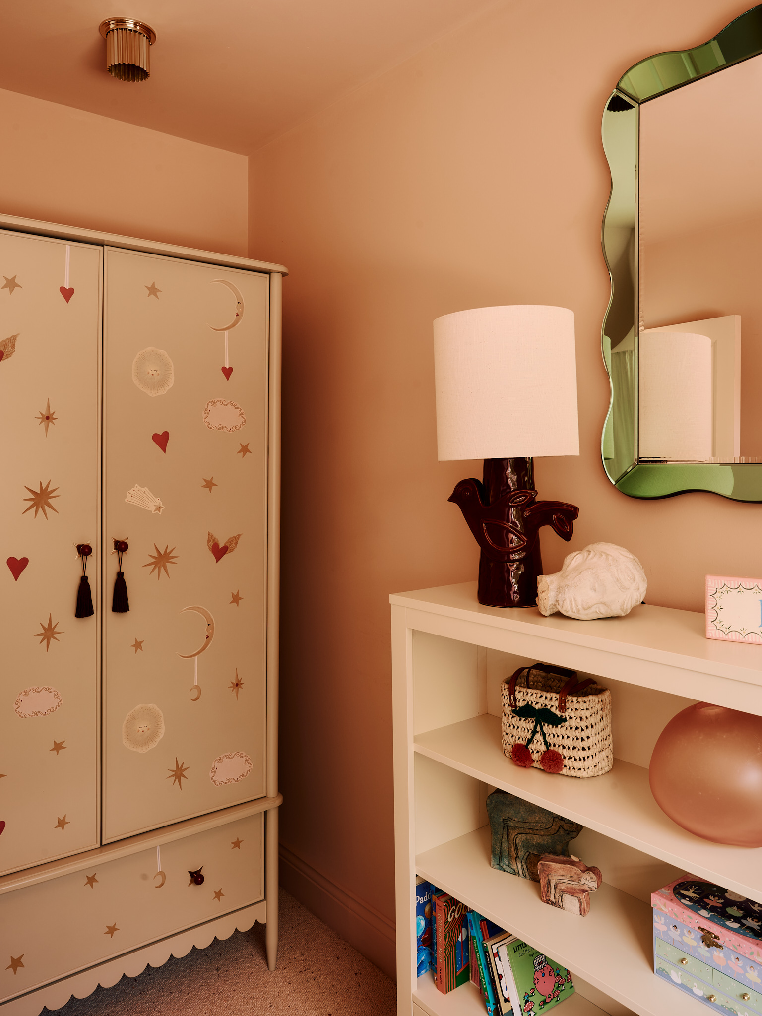 Pink room with a painted wardrobe, green mirror and display shelves at School House
