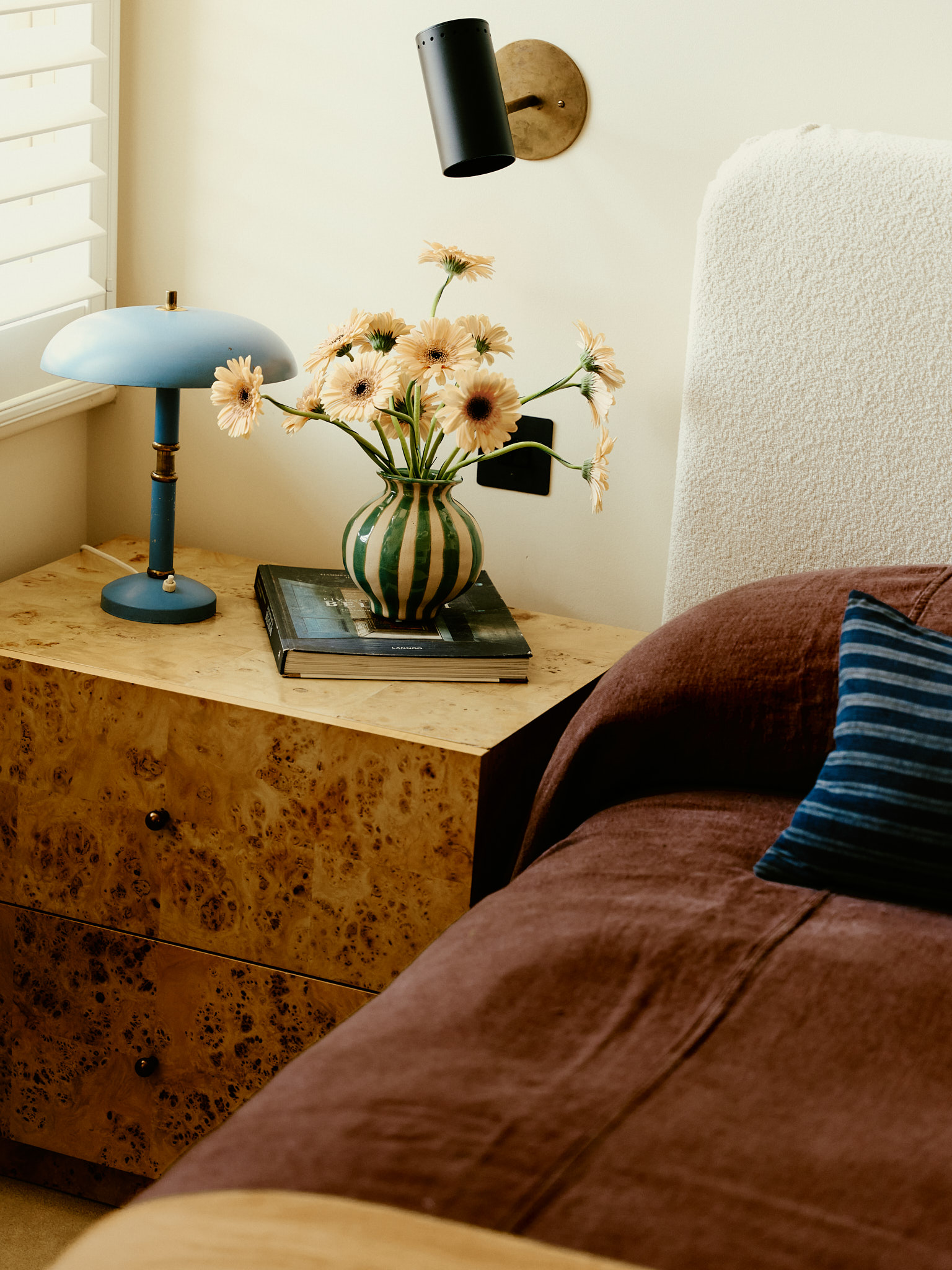 Bedside detail with a blue lamp, flowers and patterned timber cabinet at School House
