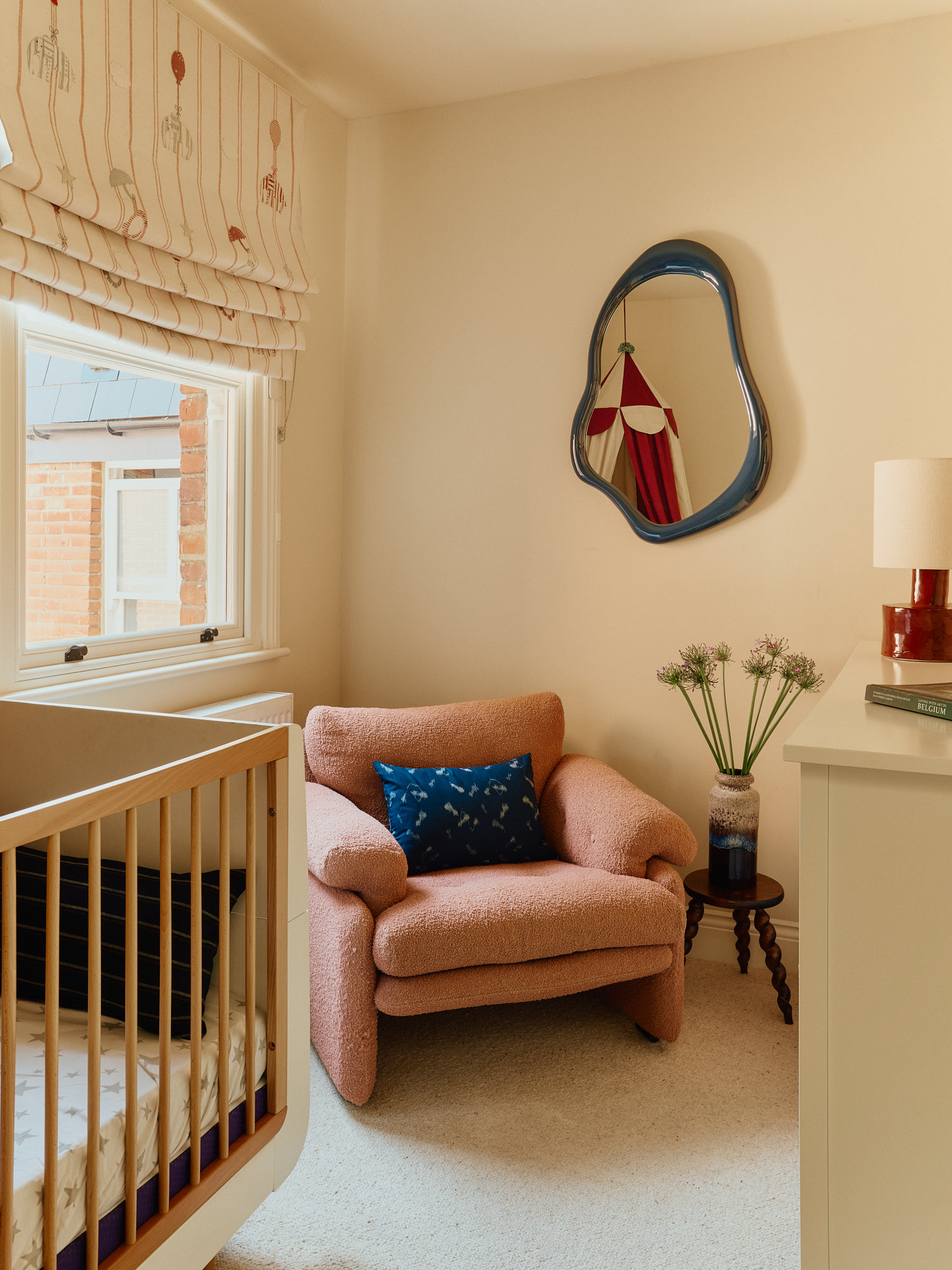 Nursery corner with a pink armchair, cot and sculptural mirror at School House
